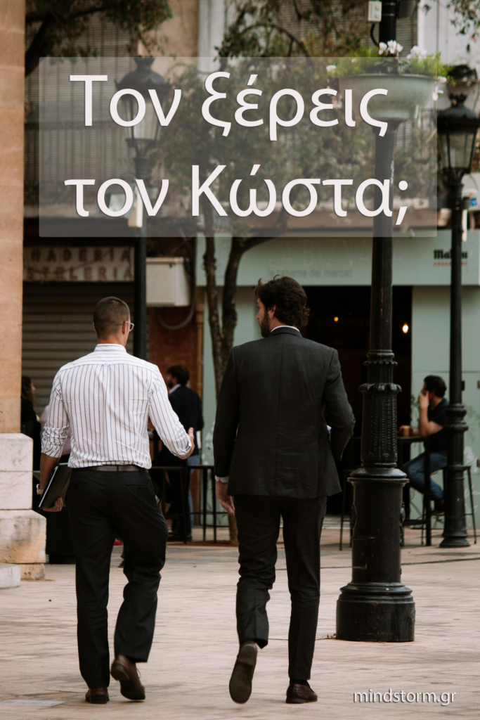 Two men in business attire walking away on a city sidewalk, seen from behind with storefronts and lampposts in the background.