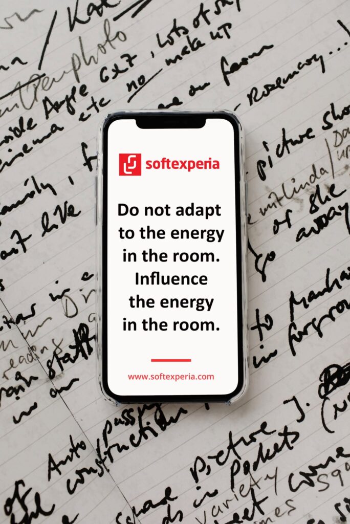 Phone displaying a Softexperia ad: red logo and the slogan 'Do not adapt to the energy in the room. Influence the energy in the room.' with the website at the bottom.
